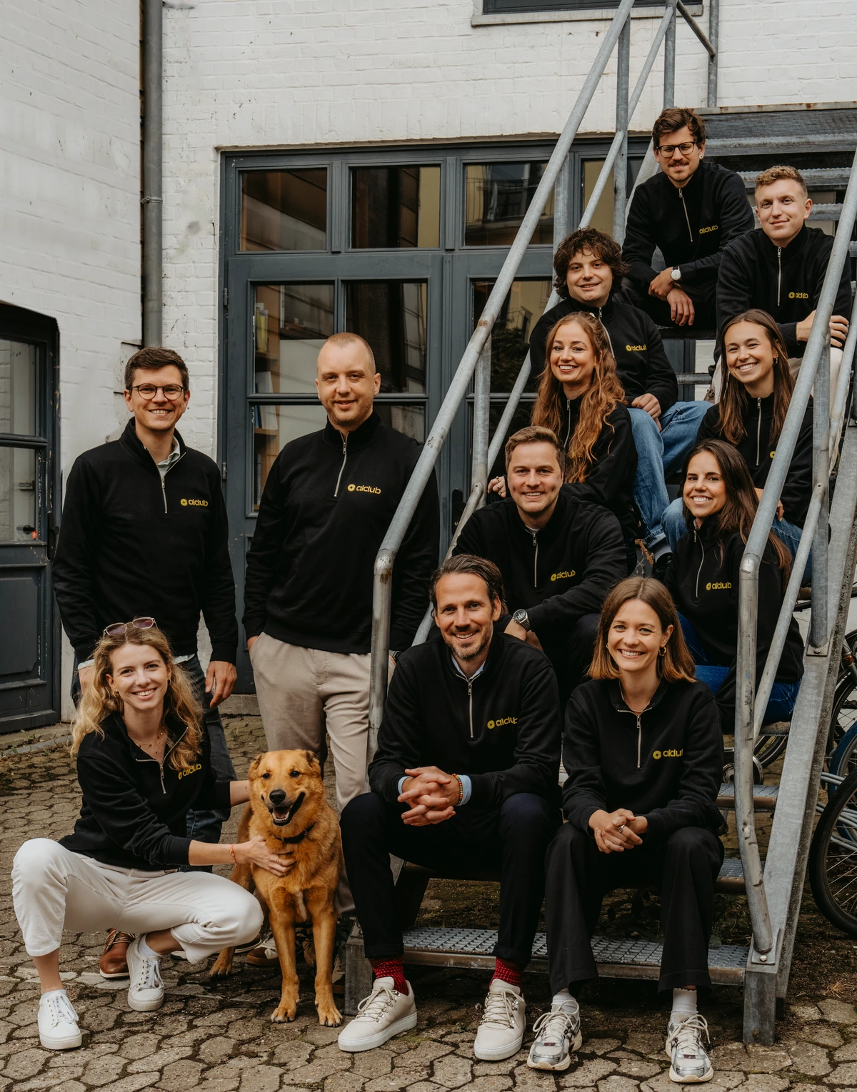 Das Team des AI Tax Club auf einer Außentreppe, vorne der Bürohund Chapito